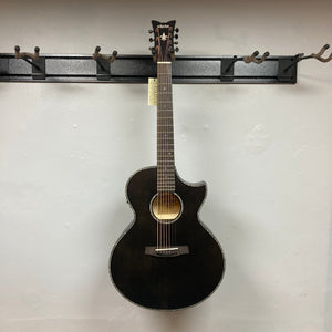 A Schecter Orleans Stage 7-String Acoustic Guitar in black, featuring a cutaway body and Engelmann spruce top, hangs on a wall-mounted rack against a plain white background. The headstock shows the Schecter brand label.