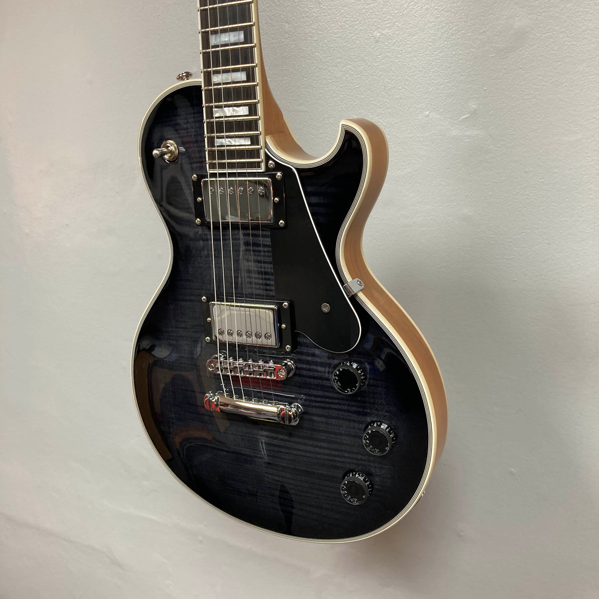 A used Schecter Solo-II Custom Trans Black Burst w/Case by Schecter hangs on a white wall, featuring chrome hardware, cream binding, black pickguard, and Pasadena USA pickups.