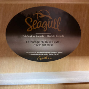 Seagull Entourage Mini Jumbo Rustic Burst MJ guitar label on wooden surface, showcasing unique wood grain and cream binding.