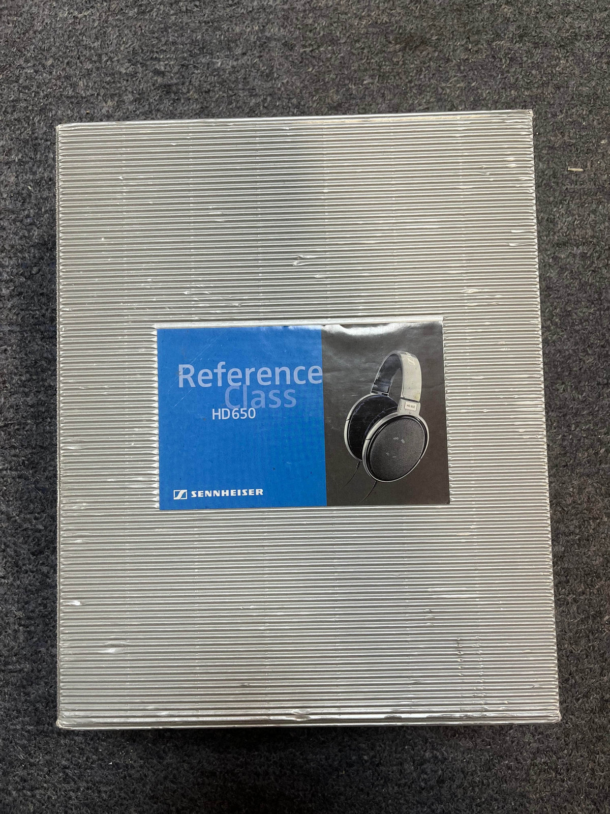 A closed box of Sennheiser HD 650 Reference Class Headphones - Preowned by Sennheiser is displayed on a gray carpeted surface.