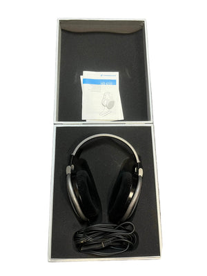 A pair of preowned Sennheiser HD 650 Reference Class open-back headphones, featuring a coiled cable and instruction manual, are neatly arranged inside an open, foam-padded box—making them an ideal option for any audiophile.