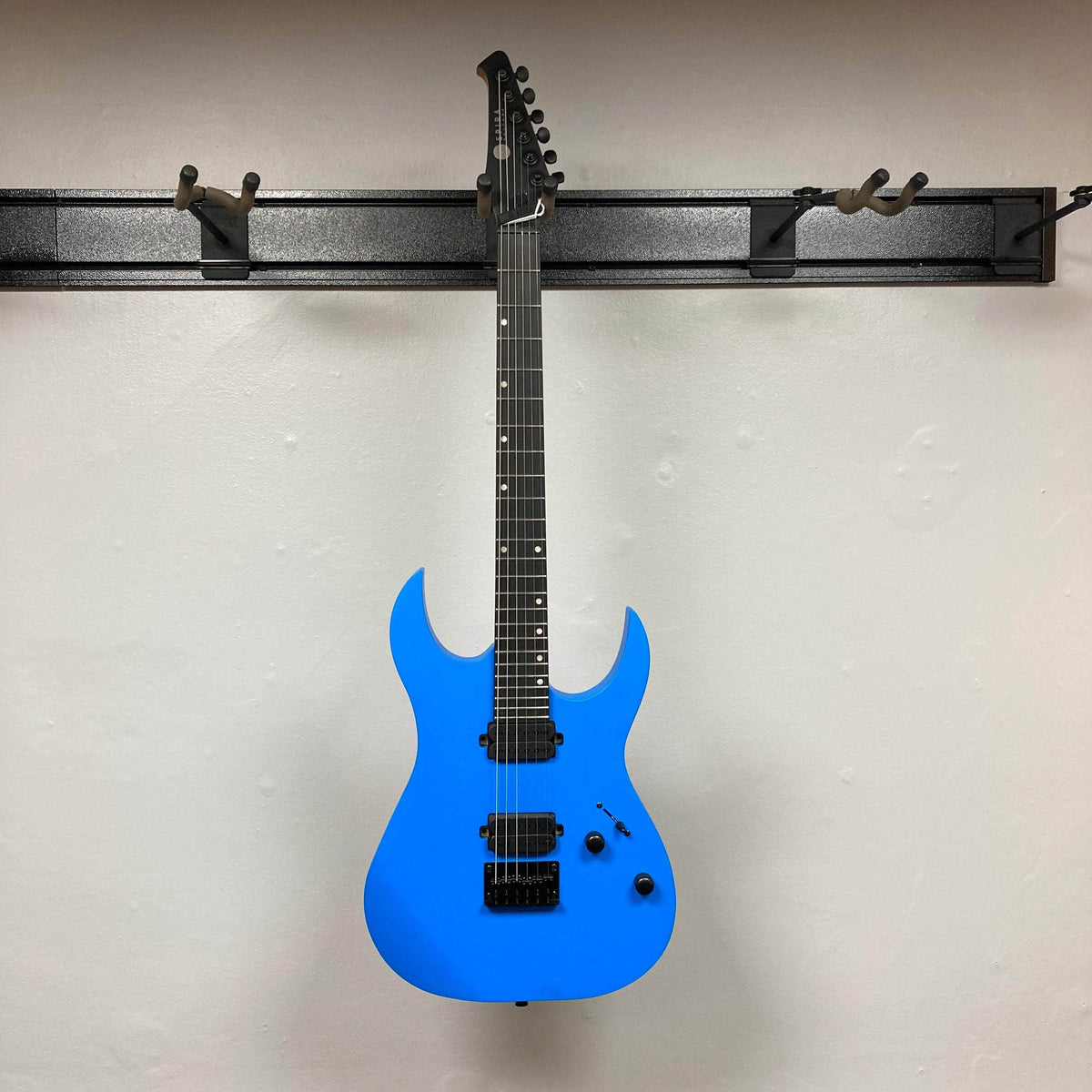 Spira S-400 MBL Electric Guitar with double-cutaway design, two humbucking pickups, fixed bridge, and black control knobs, hanging on a wall-mounted rack.