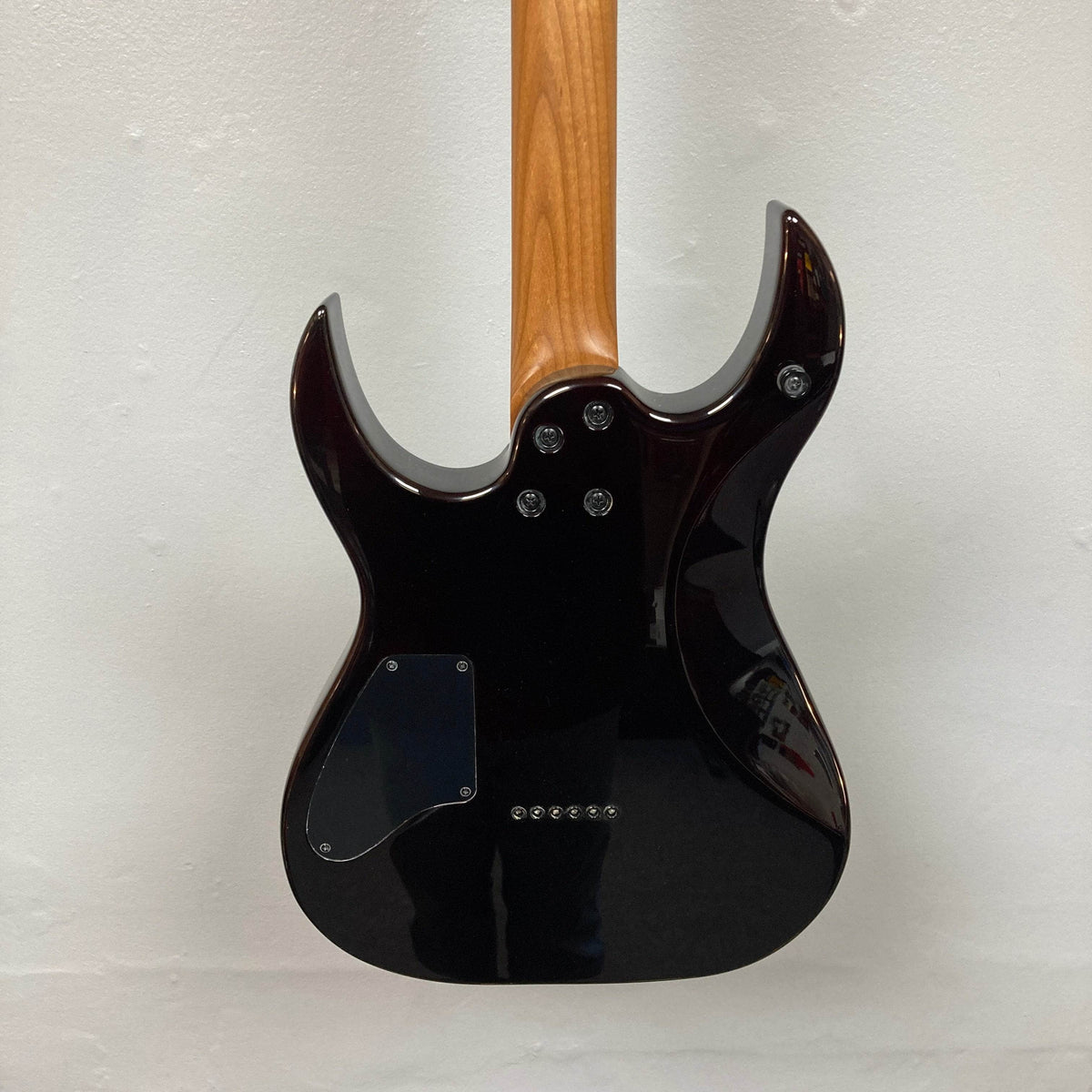 The back of the Spira S-450 Trans Green TGR electric guitar by Spira is shown, highlighting its neck joint, back plate, and string ferrules, all set against a plain light-colored wall.