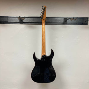 A Spira S-450 Trans Green TGR guitar by Spira hangs on a wall-mounted rack, photographed from the back to display its roasted maple neck, tuning pegs, and electronics cover against a plain white wall.