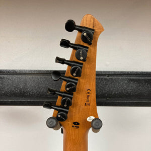 The back of a Spira S-450 Trans Green TGR's headstock features six black tuning pegs, manufacturer labels, and certification markings. Its roasted maple neck hints at quality, set against a black horizontal strip on a white wall.