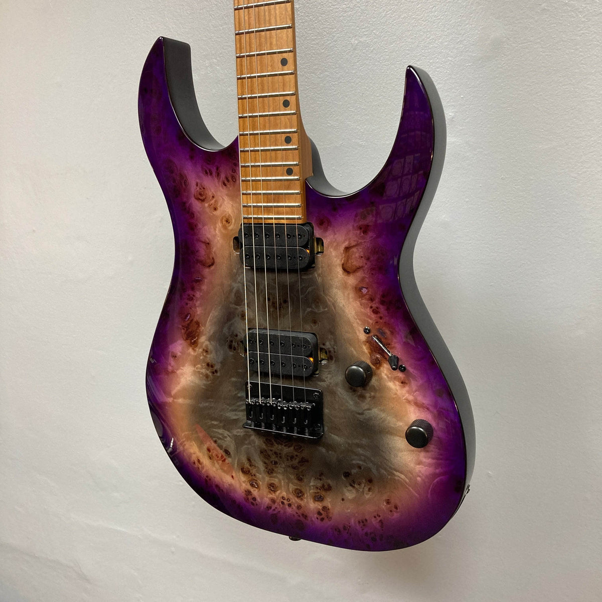 A close-up of a Spira S-450 Trans Purple TPP electric guitar by Spira, featuring Villain humbuckers, three control knobs, a maple fretboard with a modern D profile neck, and natural wood grain against a plain white wall.
