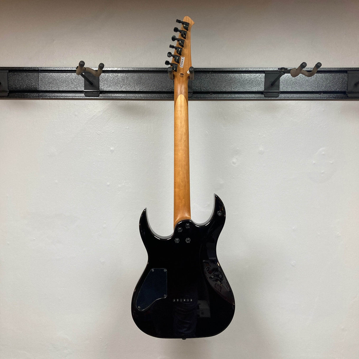 The Spira S-450 Trans Purple TPP electric guitar by Spira hangs on a wall mount, displaying its modern D profile neck, body, and neck against a plain white wall, with tuning pegs and headstock visible at the top.