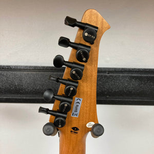 The back of the Spira S-450 Trans Purple TPP guitar headstock displays six black tuning pegs, inspection stickers, a CE mark, and a serial number against a plain wall background with a black horizontal bar.