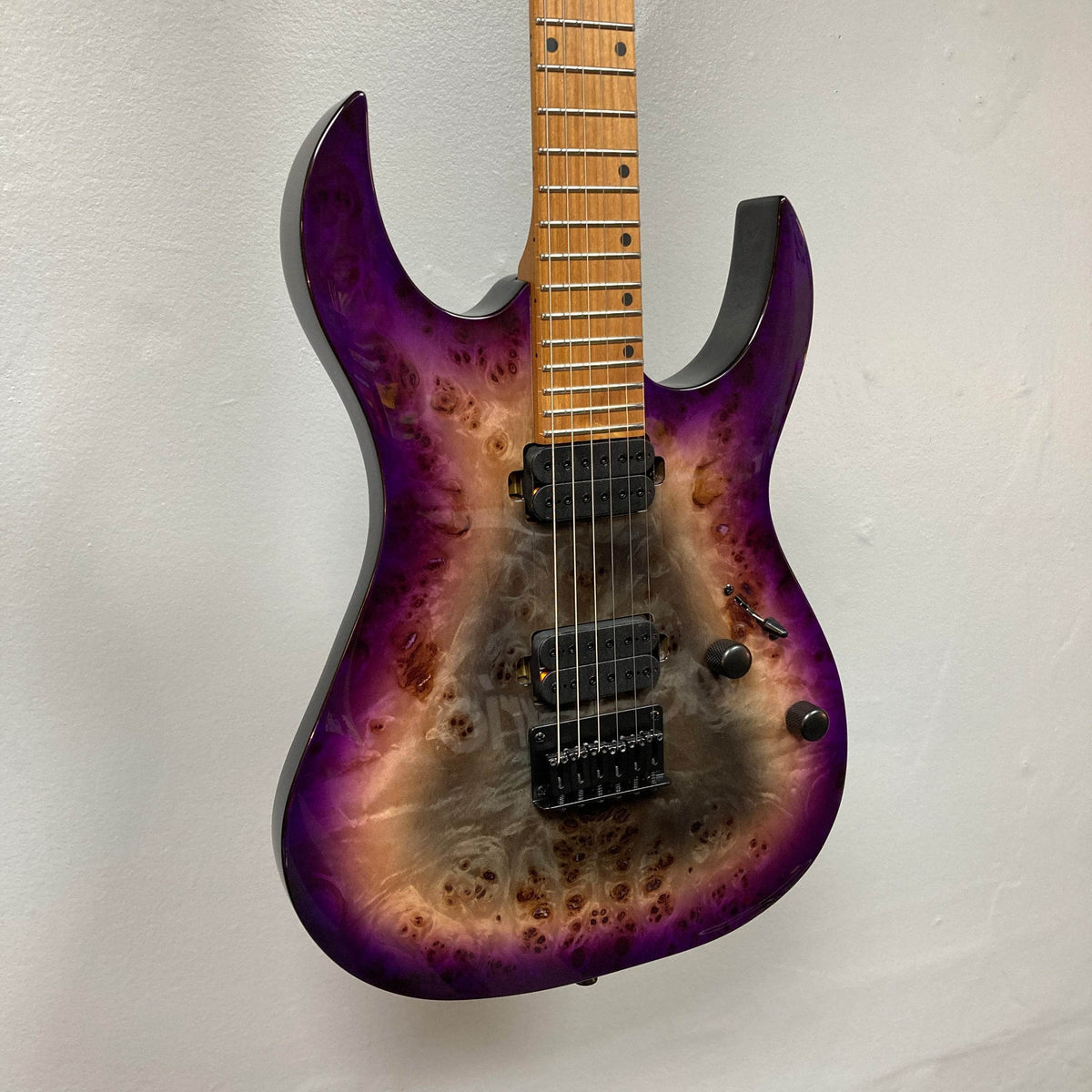 A Spira S-450 Trans Purple TPP electric guitar with a natural wood burst finish, Villain humbuckers, three control knobs, and a maple fretboard hangs on a plain white wall.