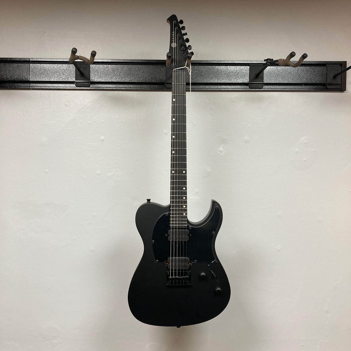 Spira T-400 MBK Electric Guitar - Black, featuring a single-cutaway, dual humbuckers, and six-inline headstock, elegantly displayed on a wall rack.
