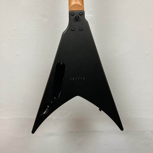 The image shows the back of a Spira V-400 MBK electric guitar by Spira, featuring a black V-shaped body and natural wood neck against a light wall, celebrated for its tuning stability.