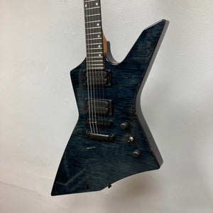 The Spira X-500 TBK E by Spira features a dark blue, angular, asymmetrical body with high-output humbuckers, black hardware, and locking tuners—an ideal metal guitar—shown against a white wall.
