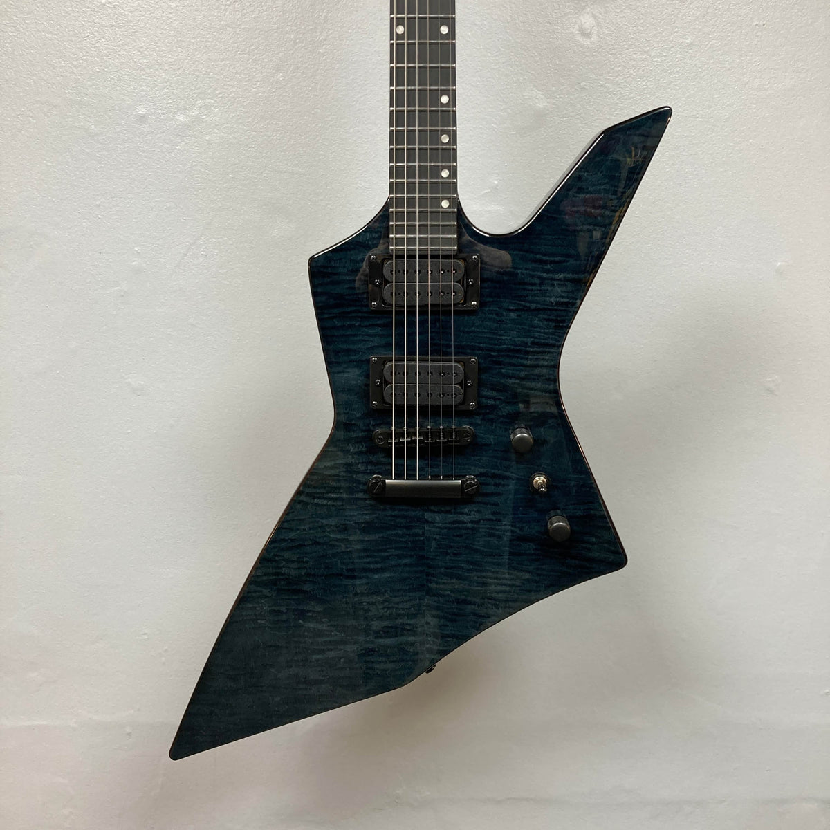 The Spira X-500 TBK E by Spira is an electric metal guitar with a sharp, angular body, dark wood finish, dual high-output humbuckers, locking tuners, and black hardware, photographed against a plain white background.