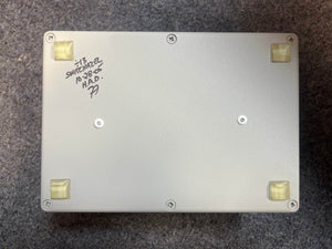 The Switchazel Boutique AB/Y Switcher with Tuner Out (Preowned) by Switchazel features a rectangular metal box, four rubber feet, and handwritten text on the bottom—perfect for guitar amp switching setups and eliminating ground loops.