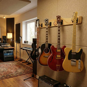 Three electric guitars hang on the A&S Crafted Products Pro-File™ Wall-Mounted Guitar Hanger in a recording studio equipped with audio gear, keyboard, microphones, and a patterned rug.