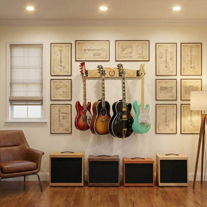Four electric guitars hang on the A&S Crafted Products Pro-File™ Wall-Mounted Guitar Hanger beneath framed technical drawings, with four amplifiers on the floor and a leather chair and lamp nearby.