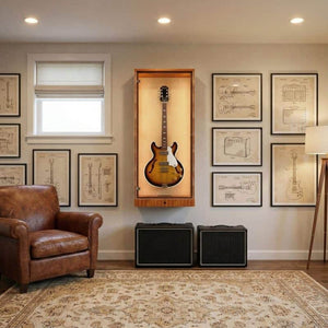 The ShowCase™ Deluxe Lockable Guitar Display Cabinet by A&S Crafted Products is wall-mounted amid technical drawings, beside a leather armchair, two amplifiers, a floor lamp, and a patterned rug in a bright room with modern LED lighting.
