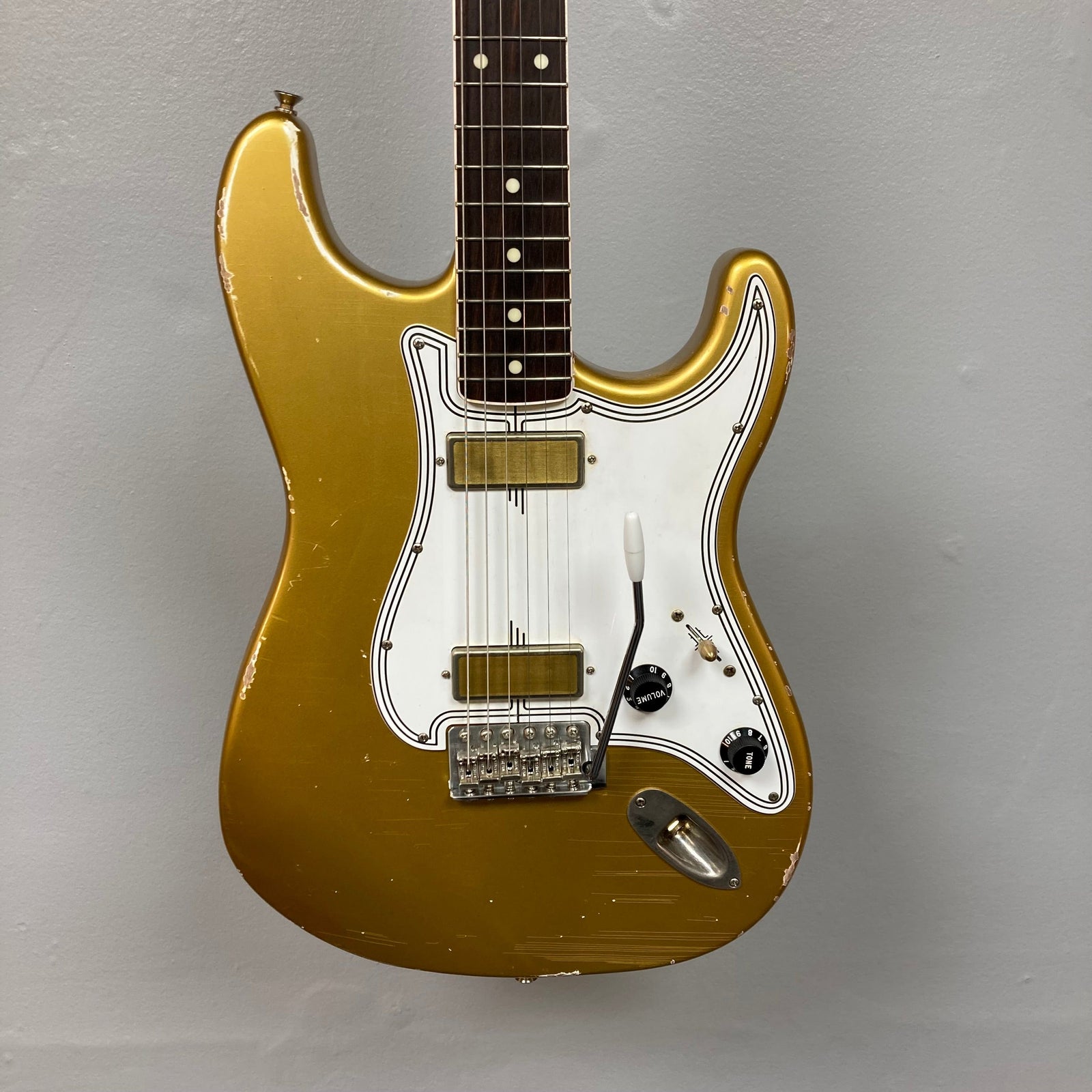 TopHat Stratavarius Aztec Gold Relic electric guitar with lacquered neck, tremolo bridge, and signature detailing, displayed on a wall. TopHat Stratavarius Aztec Gold Relic electric guitar with lacquered neck, tremolo bridge, and signature detailing, displayed on a wall.