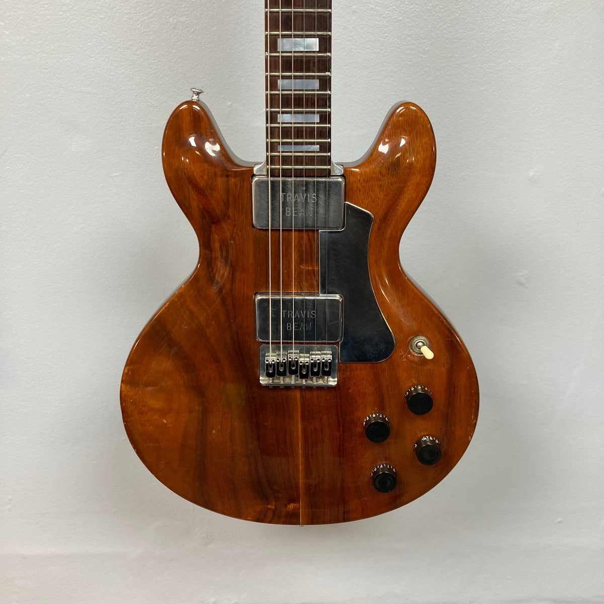 Close-up of Travis Bean TB1000A Artist Natural 1970s guitar, highlighting strings, aluminum neck, and original pickups, with vintage case visible.