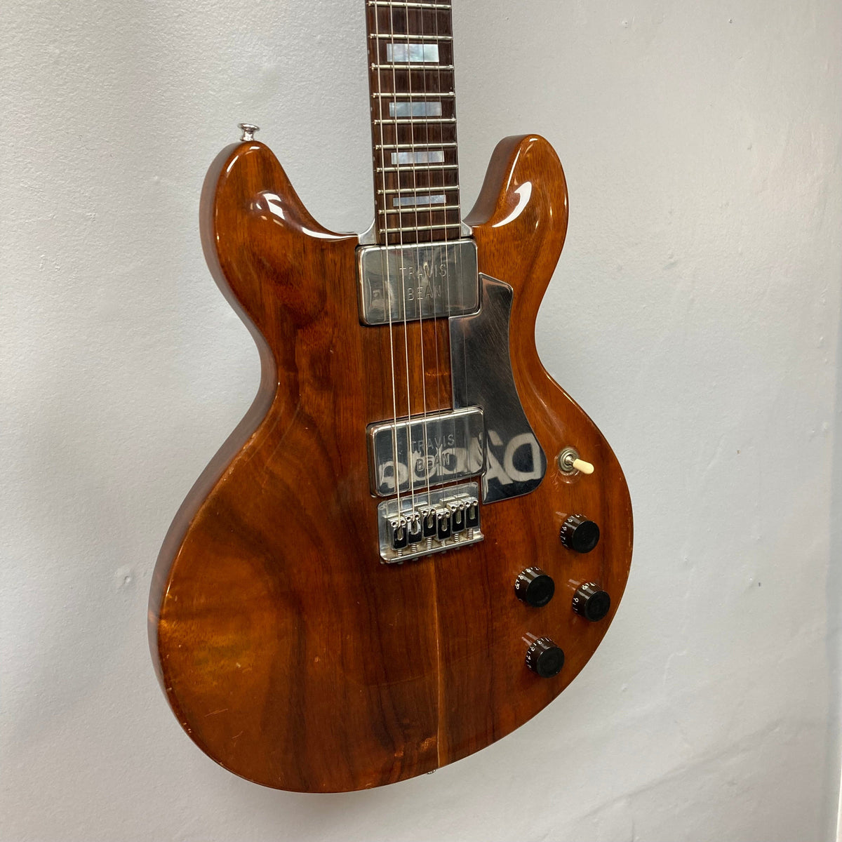 Travis Bean TB1000A Artist Natural 1970s electric guitar, brown, mounted on a wall, showcasing original components and aluminum neck, with vintage case.