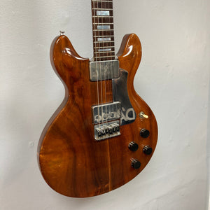 Travis Bean TB1000A Artist Natural 1970s electric guitar, brown, mounted on a wall, showcasing original components and aluminum neck, with vintage case.