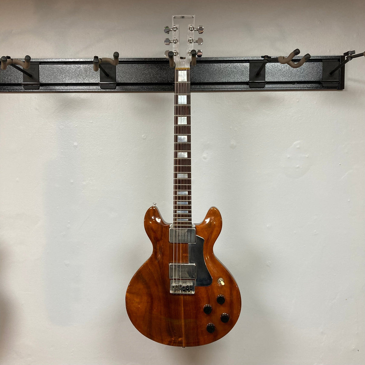 Travis Bean TB1000A Artist Natural 1970s guitar, aluminum neck, high output pickups, notable wear, displayed on a wall. Includes original vintage case.