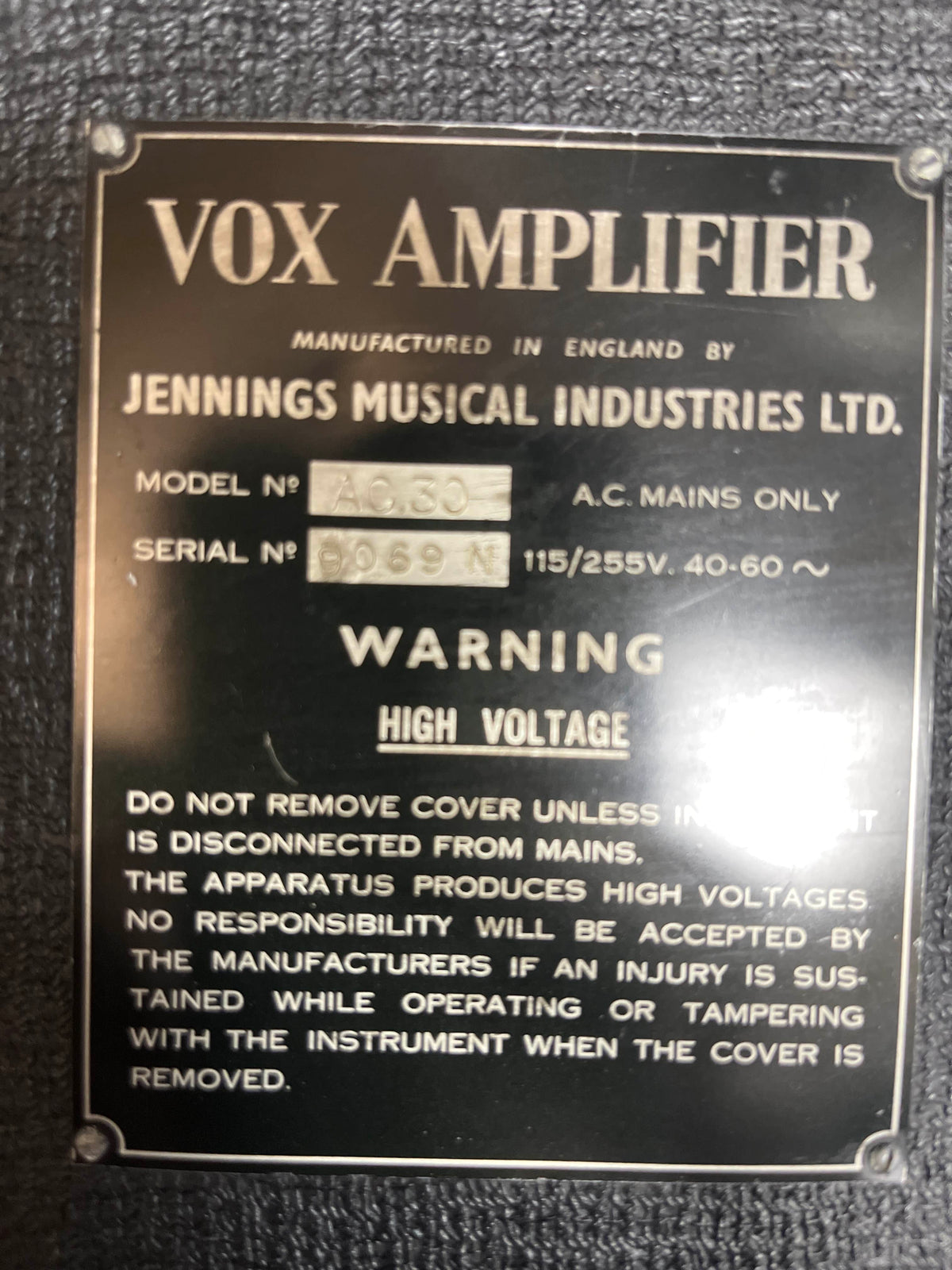 Close-up of a metal label on a Vintage 1963 Vox AC30/6 Normal by Vox, featuring model and serial numbers, voltage details, and high voltage warning; includes original JMI egg footswitch and flight case.