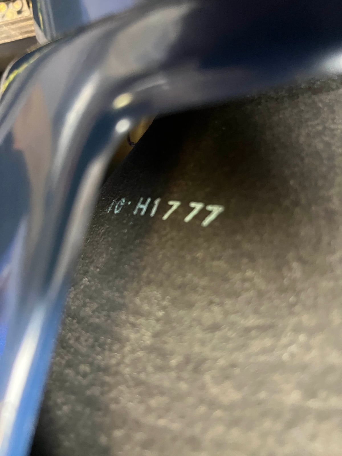 Close-up of a dark metallic surface stamped with "HC H1777," partially covered by a curved object—likely part of a Vintage 1963 Vox AC30/6 Normal amplifier by Vox, shown with its original JMI egg footswitch and flight case.