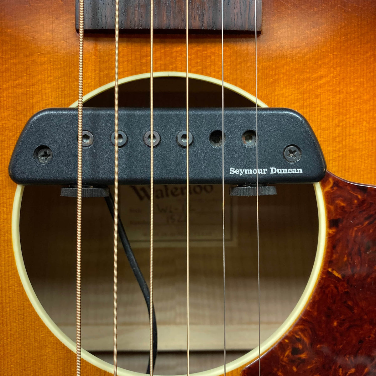 Close-up of a Waterloo WL-12 Parlor Acoustic w/Case Used Consign guitar’s sound hole, featuring a Seymour Duncan pickup. The sunburst finish and strings stand out, with the Waterloo brand label partially visible inside.