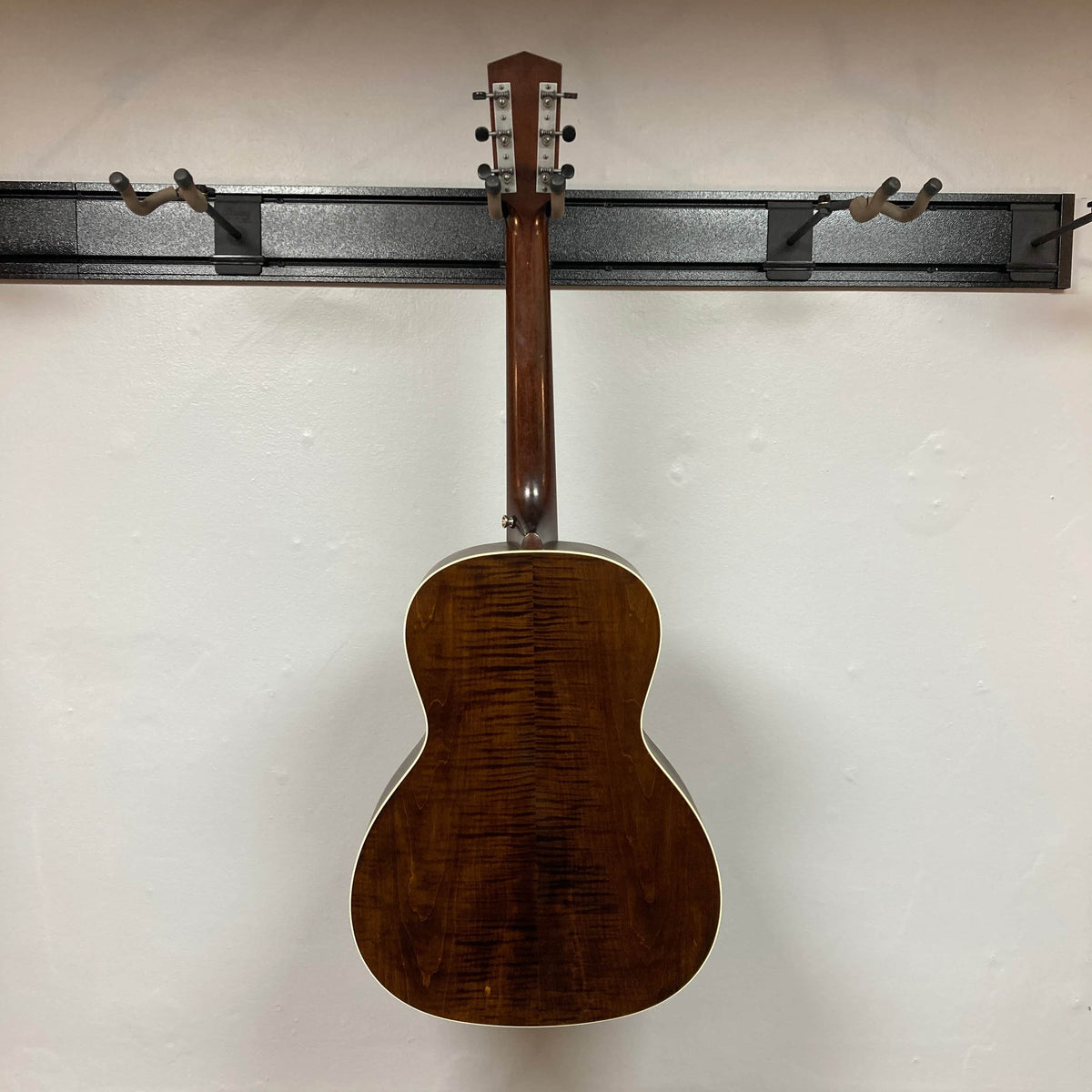 A Waterloo WL-12 Parlor Acoustic w/Case Used Consign guitar by Waterloo hangs on a black wall rack. Shot from behind, its glossy dark wood finish and white binding emphasize the visible wood grain.