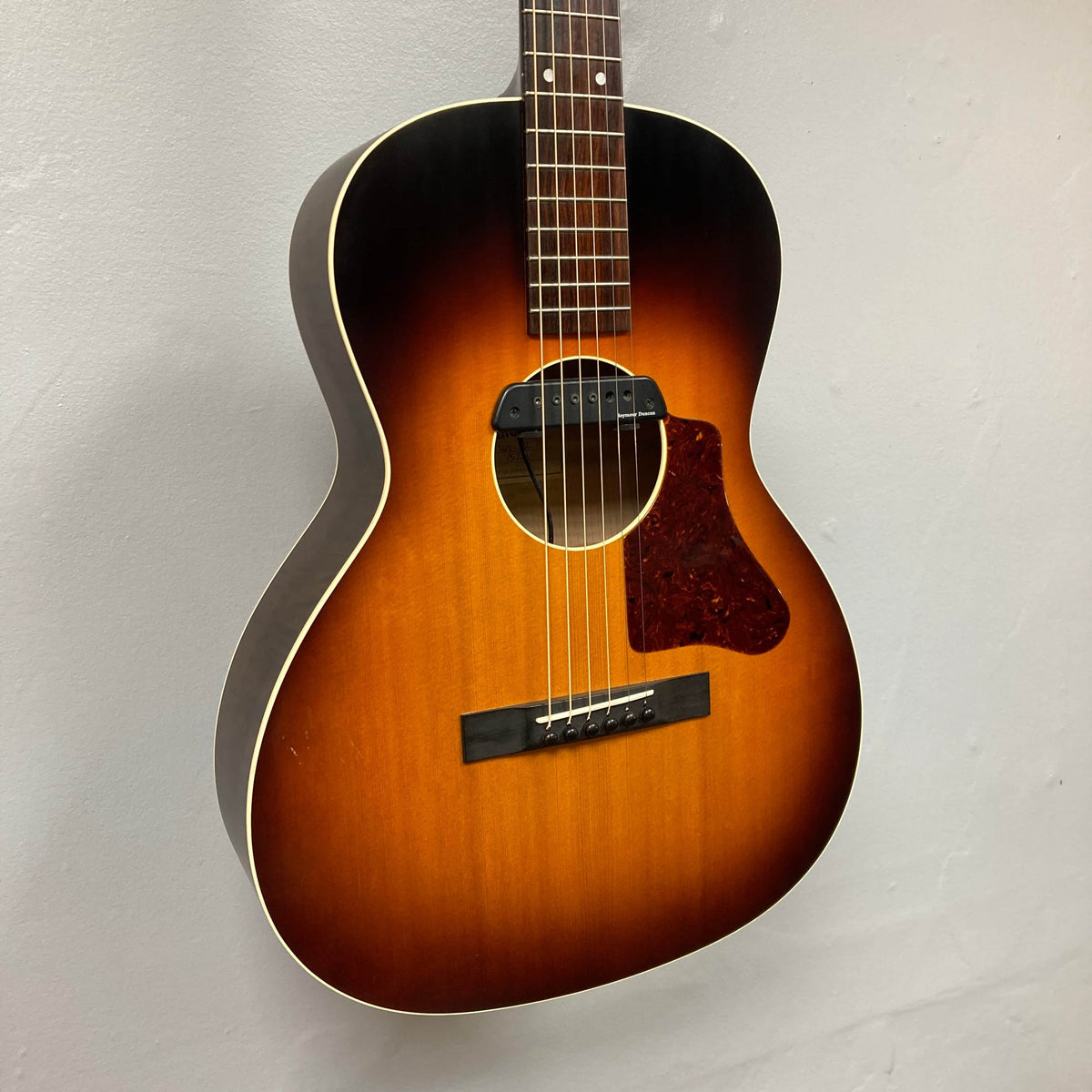 The Waterloo WL-12 Parlor Acoustic w/Case Used Consign by Waterloo is a vintage-style sunburst guitar with six strings, tortoiseshell pickguard, and white binding, perfect for classic tones and look.