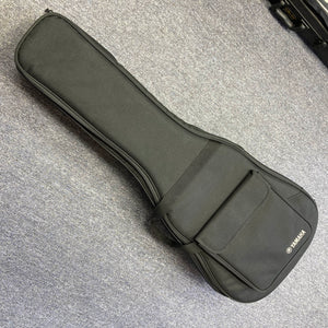 A Yamaha A3M ARE Vintage Natural Acoustic Guitar by Yamaha, featuring a solid Sitka spruce top and SRT2 pickup system, along with its included hard bag, is resting on a gray carpeted floor. The hard bag offers a convenient front pocket for storing accessories.