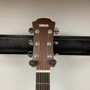 A close-up of the headstock of a Yamaha A3M ARE Vintage Natural Acoustic Guitar w/Hard Bag Used showcases the tuning pegs and Yamaha logo as it rests on a wall hanger. The image draws attention to premium features such as its solid mahogany construction and suggests innovative elements like the advanced SRT2 pickup system.