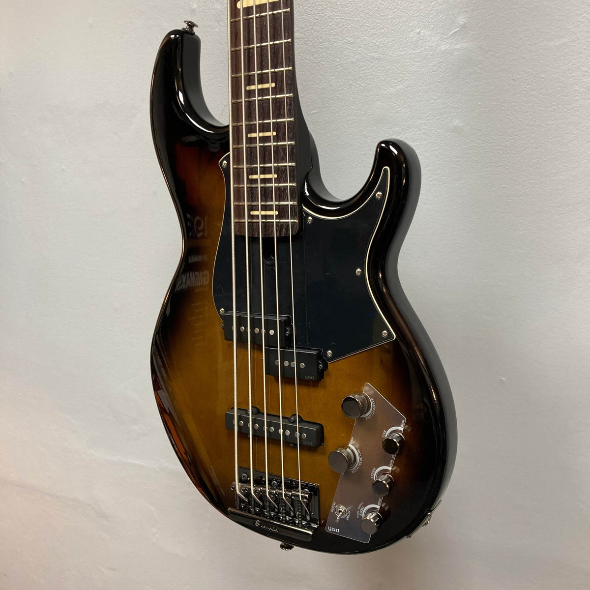 A close-up of a Yamaha BB735A Electric 5-String Bass in Coffee Sunburst (Blem Discount) hanging on a wall, featuring two pickups, four control knobs, a pickguard, and an adjustable bridge.