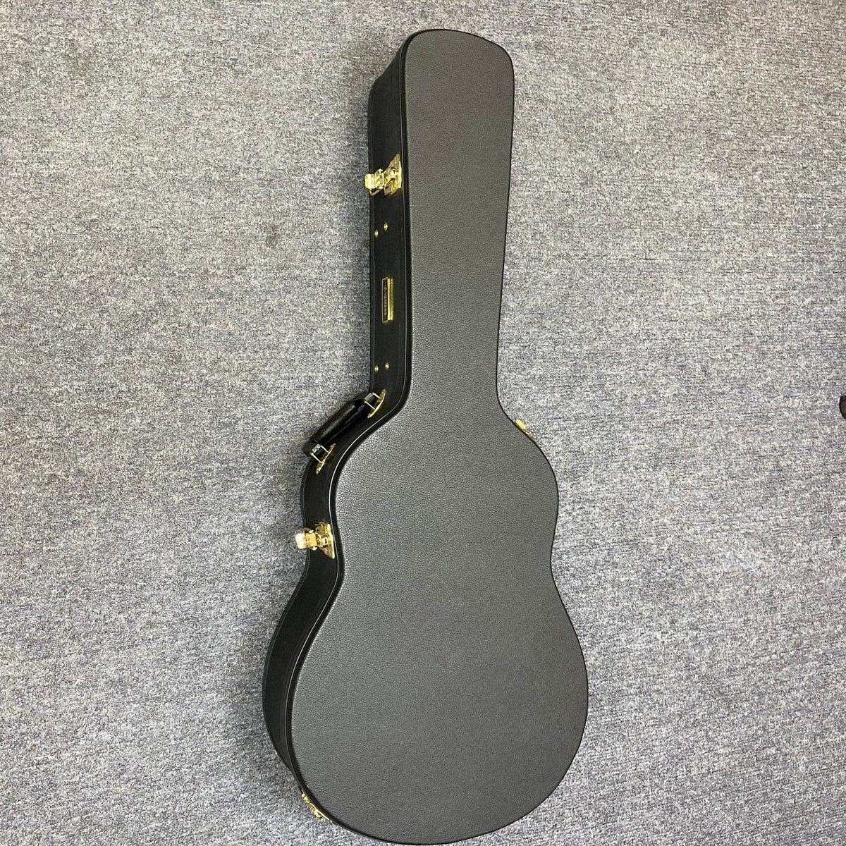 A Yamaha FSX5 Red Label natural acoustic-electric guitar in its closed, black hard-shell case with gold latches is lying on a gray carpeted floor.
