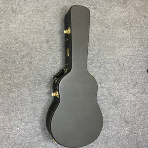A Yamaha FSX5 Red Label natural acoustic-electric guitar in its closed, black hard-shell case with gold latches is lying on a gray carpeted floor.