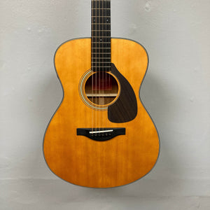 The Yamaha FSX5 Satin Red Label Natural Made In Japan w/Case, an acoustic electric guitar by Yamaha, is shown front-facing against a plain light gray wall, highlighting its body, sound hole, pickguard, and part of the neck.