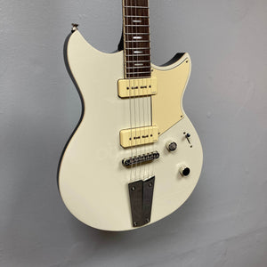 A Yamaha Revstar Standard RSS02T electric guitar in Vintage White with P90 pickups, cream pickguard, three control knobs, and chrome bridge hangs against a plain gray wall. Includes gigbag.