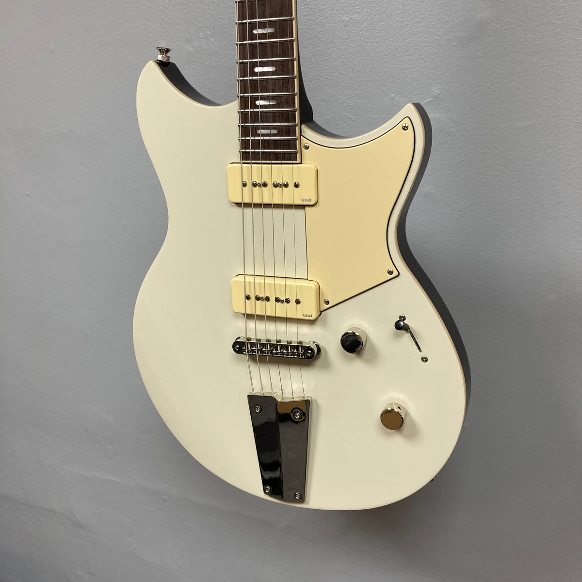 A Yamaha Revstar Standard RSS02T electric guitar in Vintage White, featuring a chambered mahogany body, dual P90 pickups, pickguard, three control knobs, and chrome tailpiece, shown against a plain gray wall. Includes gigbag.