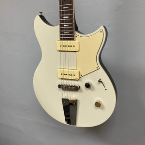 A Yamaha Revstar Standard RSS02T electric guitar in Vintage White, featuring a chambered mahogany body, dual P90 pickups, pickguard, three control knobs, and chrome tailpiece, shown against a plain gray wall. Includes gigbag.