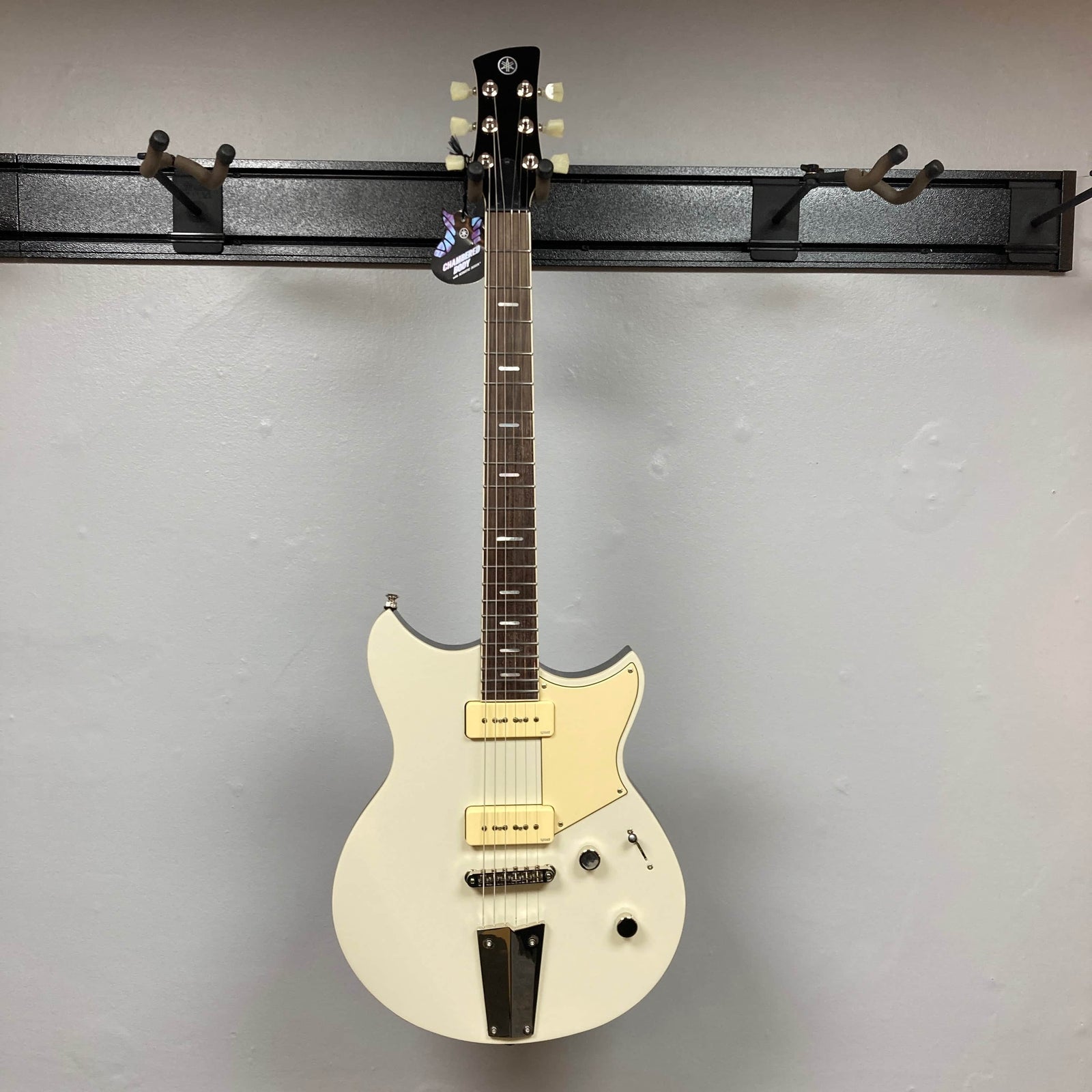 A Yamaha Revstar Standard RSS02T Vintage White electric guitar with P90 pickups and a chambered mahogany body hangs against a plain gray wall. Comes with a gigbag. A Yamaha Revstar Standard RSS02T Vintage White electric guitar with P90 pickups and a chambered mahogany body hangs against a plain gray wall. Comes with a gigbag.