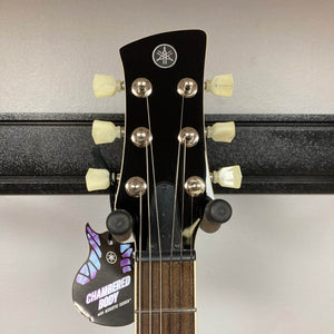 Close-up of the Yamaha Revstar Standard RSS02T Vintage White headstock with six tuners, a "Chambered Body with Acoustic Design" tag, chambered mahogany body detail, and fretboard—all displayed on a wall hanger.