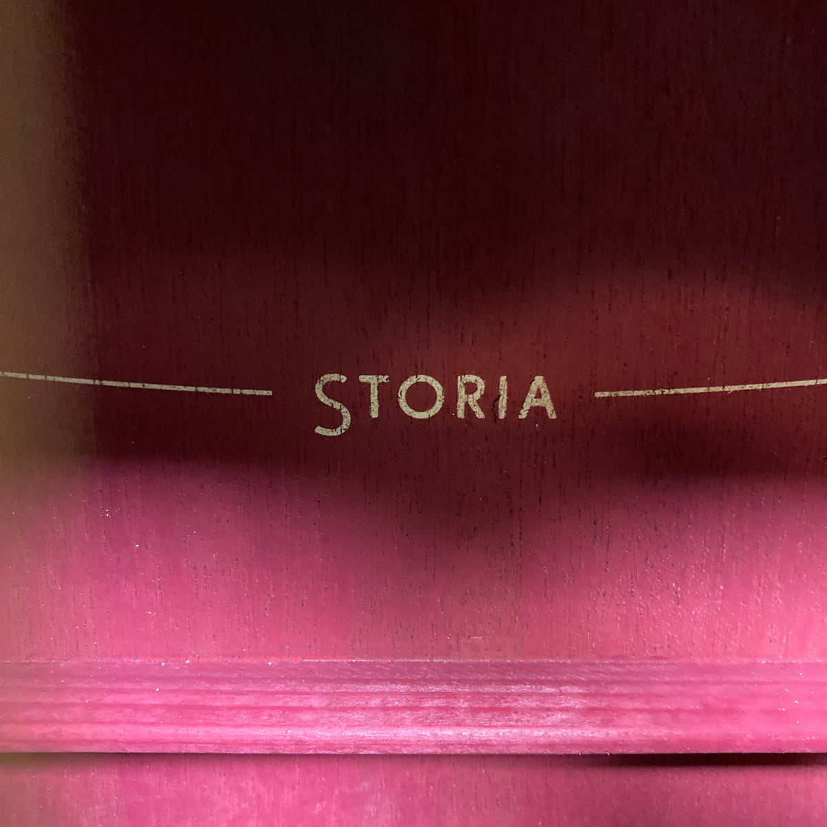 Close-up of "STORIA" in gold letters on a reddish wood, showcasing the Yamaha Storia III Solid Mahogany Top Concert guitar’s solid mahogany top.