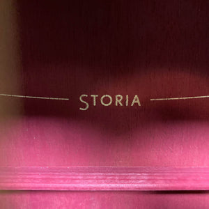 Close-up of "STORIA" in gold letters on a reddish wood, showcasing the Yamaha Storia III Solid Mahogany Top Concert guitar’s solid mahogany top.