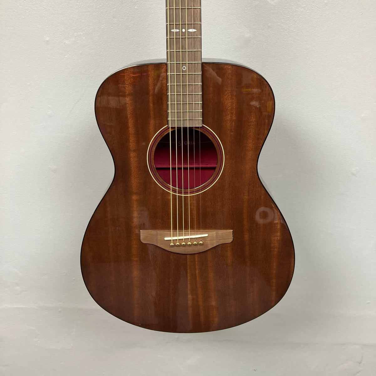 A Yamaha Storia III Solid Mahogany Top Concert guitar with a glossy finish hangs against a plain white wall.