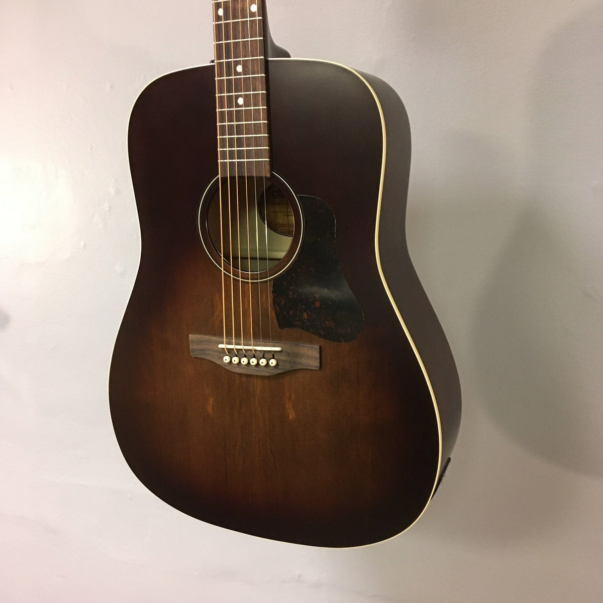 Art & Lutherie Americana Bourbon Burst Presys II guitar on a wall, showcasing its detailed craftsmanship and design.