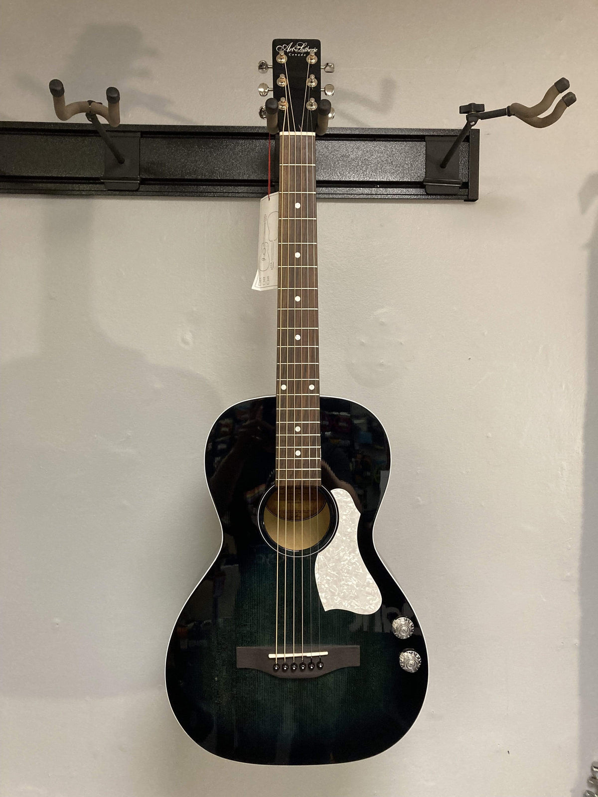 An Art & Lutherie Roadhouse HG Indigo Burst Q-Discrete acoustic guitar with an indigo burst finish hangs on a wall-mounted display rack.