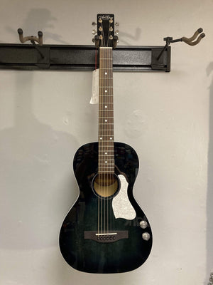 An Art & Lutherie Roadhouse HG Indigo Burst Q-Discrete acoustic guitar with an indigo burst finish hangs on a wall-mounted display rack.