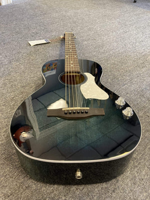 The Art & Lutherie Roadhouse HG Indigo Burst Q-Discrete, an acoustic-electric parlor guitar with an indigo burst finish, rests on a gray carpeted floor, displaying its body, bridge, knobs, and partial neck.