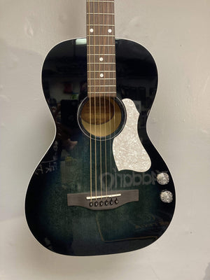 An Art & Lutherie Roadhouse HG Indigo Burst Q-Discrete parlor guitar with two control knobs and a white pickguard hangs on a light-colored wall.